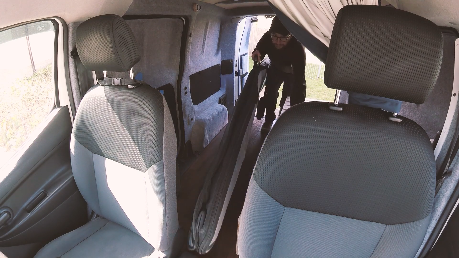 A man putting a surfboard through the gap of the front seats of a van